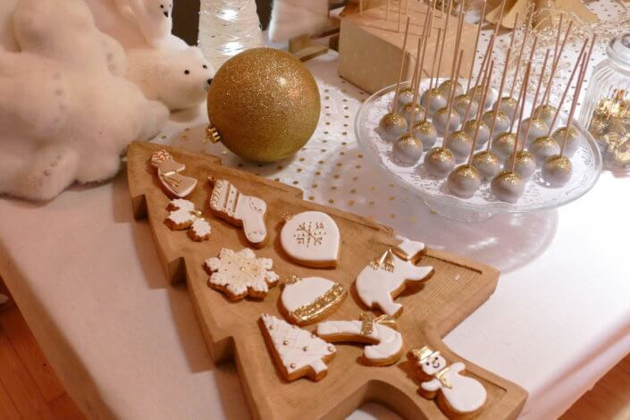 Soirée de Noël Adopt par Studio Candy avec une grande table de Noël décorée en or et blanc. Cakepops au chocolat, cupcakes, sapins meringue, sablés de Noël et corbeille de fruits et cocktail salé avec verrines, grazing platters, cônes garnis