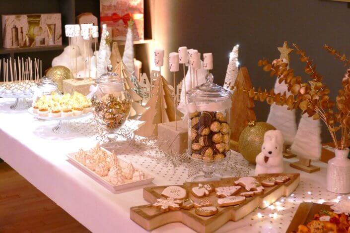 Soirée de Noël Adopt par Studio Candy avec une grande table de Noël décorée en or et blanc. Cakepops au chocolat, cupcakes, sapins meringue, sablés de Noël et corbeille de fruits et cocktail salé avec verrines, grazing platters, cônes garnis