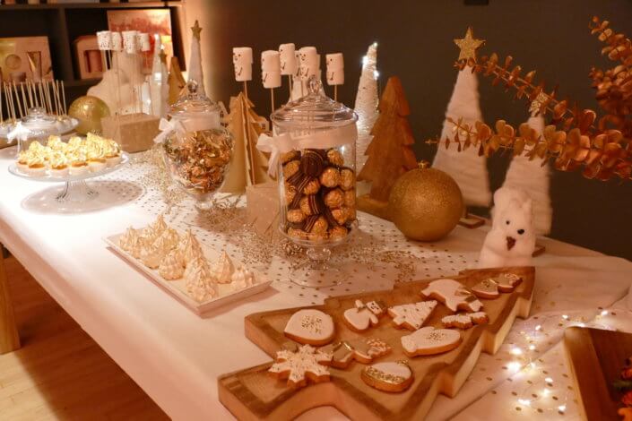 Soirée de Noël Adopt par Studio Candy avec une grande table de Noël décorée en or et blanc. Cakepops au chocolat, cupcakes, sapins meringue, sablés de Noël et corbeille de fruits et cocktail salé avec verrines, grazing platters, cônes garnis