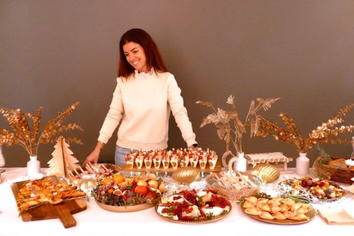 Soirée de Noël Adopt par Studio Candy avec une grande table de Noël décorée en or et blanc. Cakepops au chocolat, cupcackes, sapins meringue, sablés de Noël et corbeille de fruits et cocktail salé avec verrines, grazing platters, cônes garnis