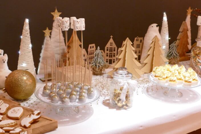 Soirée de Noël Adopt par Studio Candy avec une grande table de Noël décorée en or et blanc. Cakepops au chocolat, cupcackes, sapins meringue, sablés de Noël et corbeille de fruits et cocktail salé avec verrines, grazing platters, cônes garnis