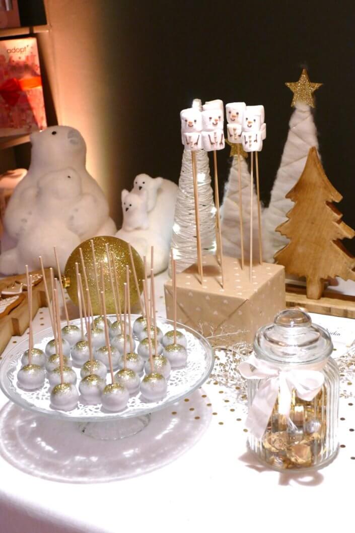 Soirée de Noël Adopt par Studio Candy avec une grande table de Noël décorée en or et blanc. Cakepops au chocolat, cupcakes, sapins meringue, sablés de Noël et corbeille de fruits et cocktail salé avec verrines, grazing platters, cônes garnis