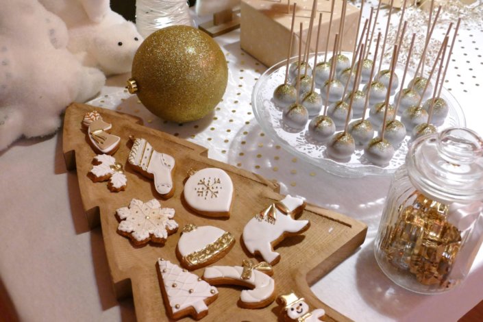 Soirée de Noël Adopt par Studio Candy avec une grande table de Noël décorée en or et blanc. Cakepops au chocolat, cupcakes, sapins meringue, sablés de Noël et corbeille de fruits et cocktail salé avec verrines, grazing platters, cônes garnis