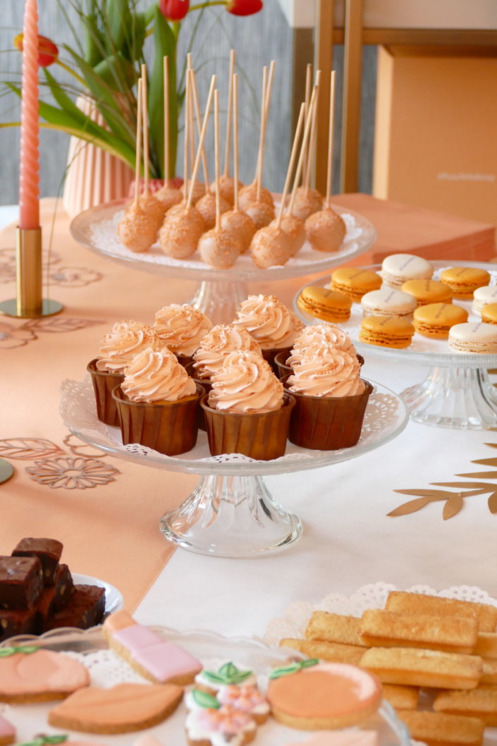 Evénement pêche Estée Lauder par Studio Candy avec table sur mesure décorée avec cakepops et cupcakes pêches, sablés décorés personnalisés, planches cocktail estivales et fontaines à boissons