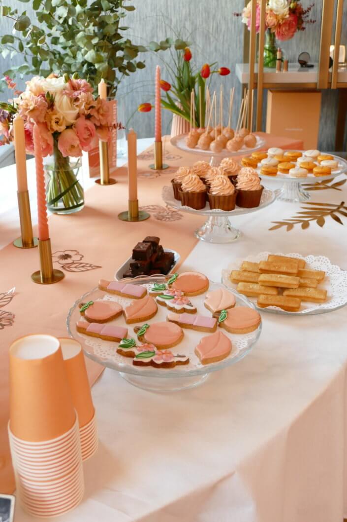 Evénement pêche Estée Lauder par Studio Candy avec table sur mesure décorée avec cakepops et cupcakes pêches, sablés décorés personnalisés, planches cocktail estivales et fontaines à boissons