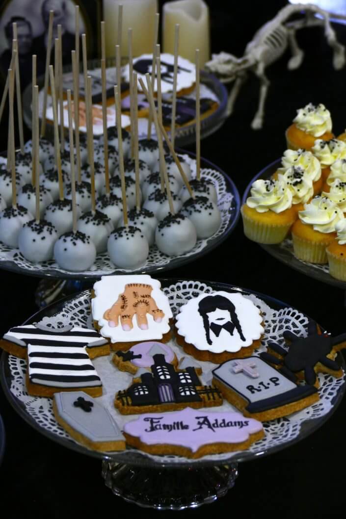 Goûter lancement film la famille addams par Studio Candy avec une scénographie sur mesure et des pâtisseries en noir et blanc, sablés décorés manoir, la chose, nattes de Mercredi et cercueil