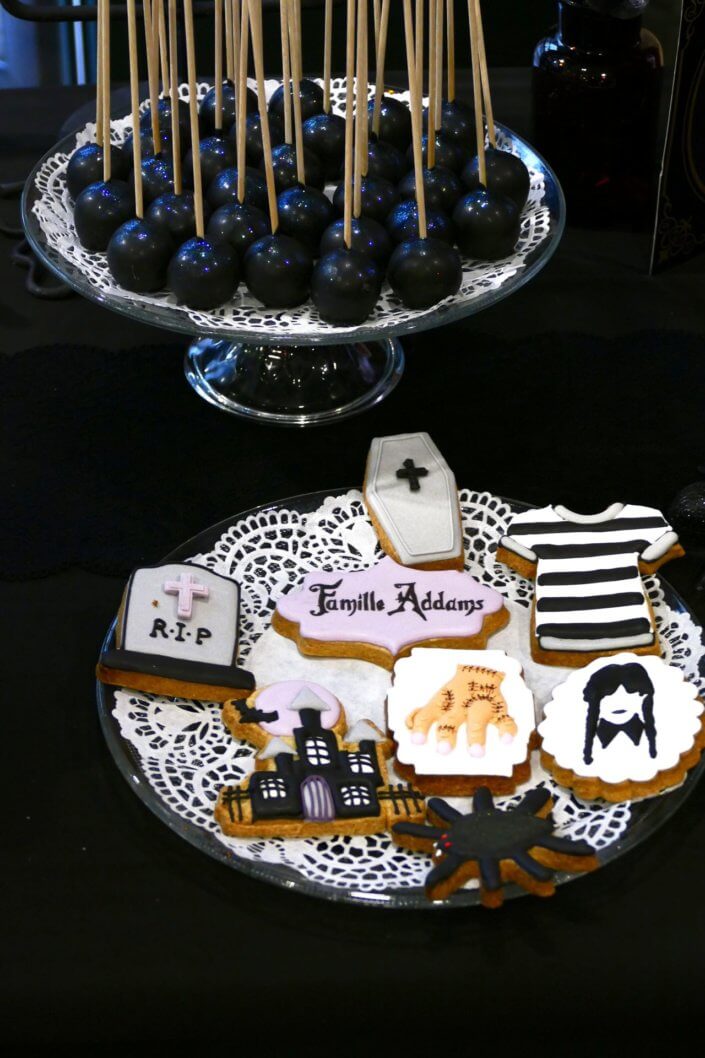Goûter lancement film la famille addams par Studio Candy avec une scénographie sur mesure et des pâtisseries en noir et blanc, sablés décorés manoir, la chose, nattes de Mercredi et cercueil