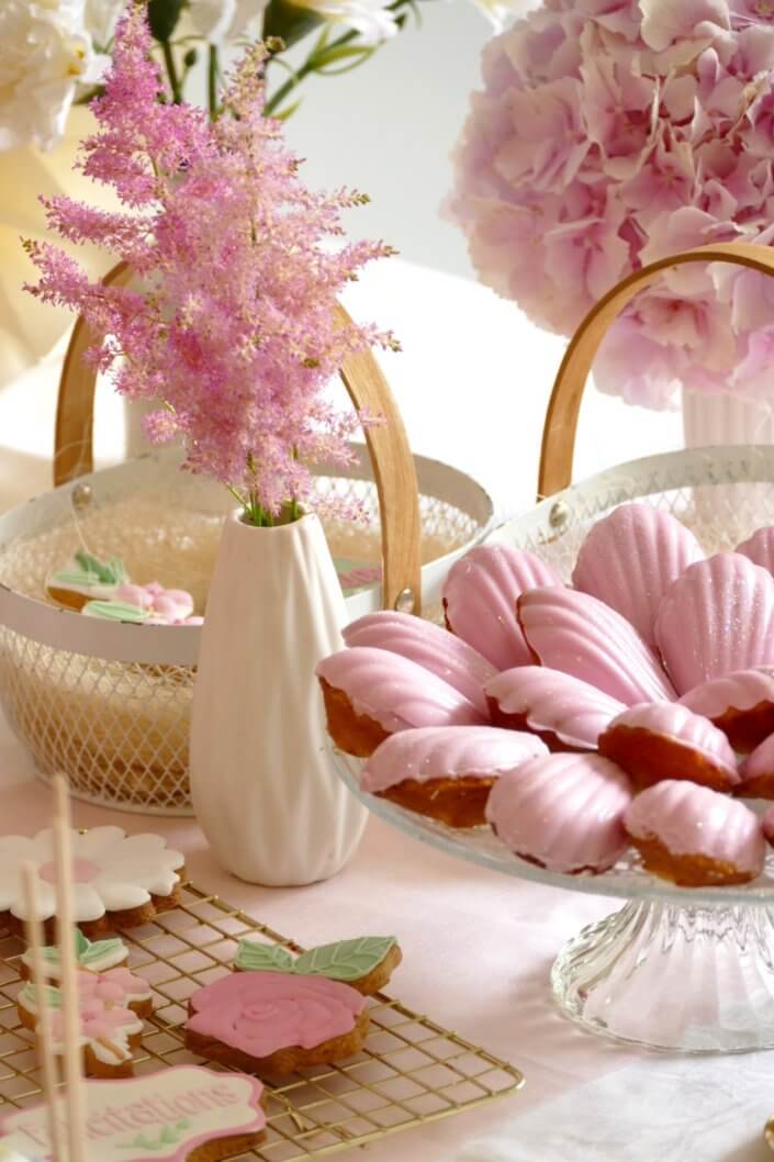 Goûter fleuri en rose et blanc réalisé sur mesure par studio candy avec des pâtisseries personnalisées, mini cupcakes, madeleines à coque rose, gaufres, sablés décorés, et scénographie printanière