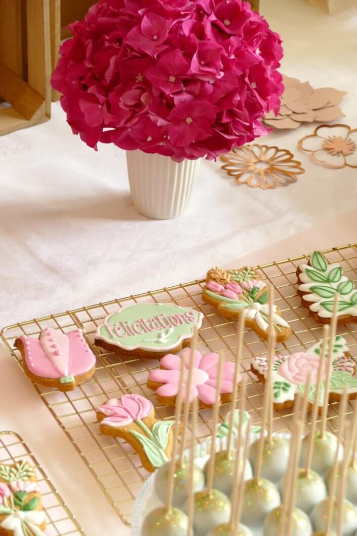 Goûter fleuri en rose et blanc réalisé sur mesure par studio candy avec des pâtisseries personnalisées, mini cupcakes, madeleines à coque rose, gaufres, sablés décorés, et scénographie printanière