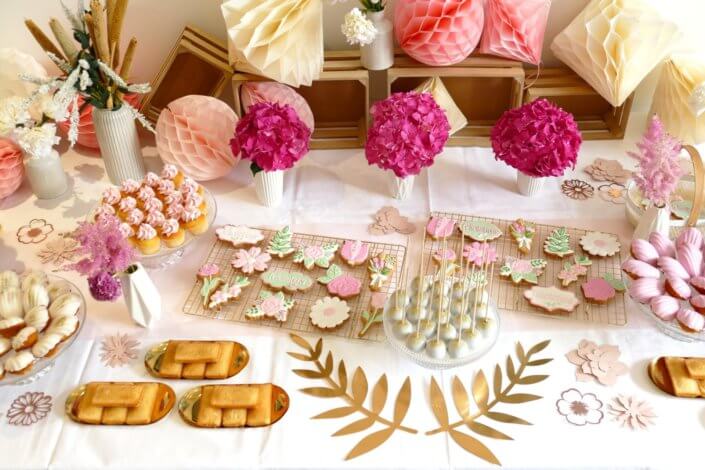 Goûter fleuri en rose et blanc réalisé sur mesure par studio candy avec des pâtisseries personnalisées, mini cupcakes, madeleines à coque rose, gaufres, sablés décorés, et scénographie printanière