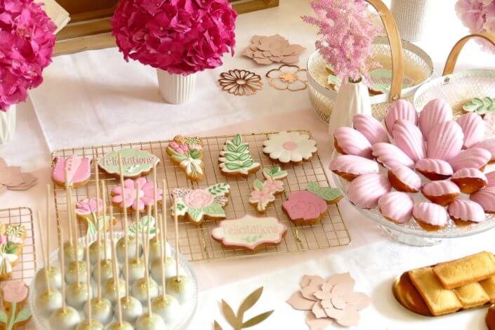 Goûter fleuri en rose et blanc réalisé sur mesure par studio candy avec des pâtisseries personnalisées, mini cupcakes, madeleines à coque rose, gaufres, sablés décorés, et scénographie printanière