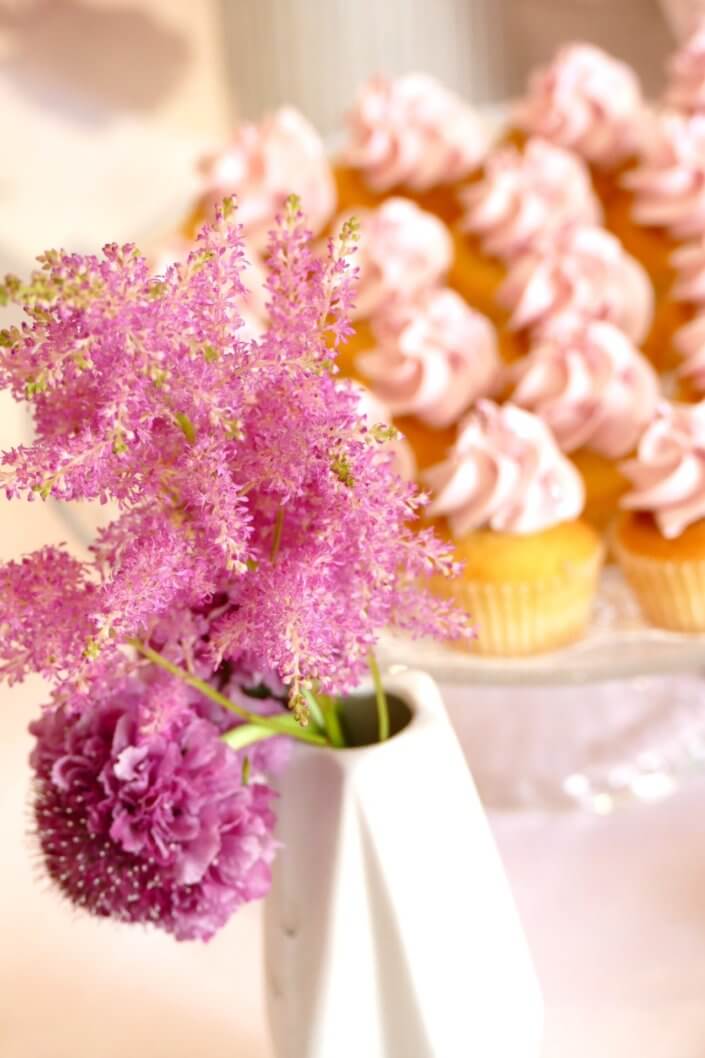 Goûter fleuri en rose et blanc réalisé sur mesure par studio candy avec des pâtisseries personnalisées, mini cupcakes, madeleines à coque rose, gaufres, sablés décorés, et scénographie printanière