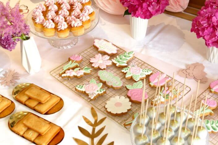 Goûter fleuri en rose et blanc réalisé sur mesure par studio candy avec des pâtisseries personnalisées, mini cupcakes, madeleines à coque rose, gaufres, sablés décorés, et scénographie printanière