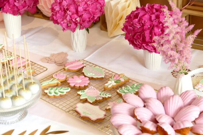 Goûter fleuri en rose et blanc réalisé sur mesure par studio candy avec des pâtisseries personnalisées, mini cupcakes, madeleines à coque rose, gaufres, sablés décorés, et scénographie printanière