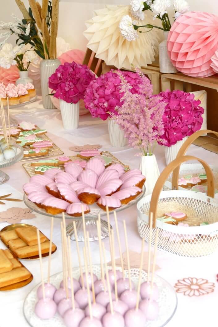 Goûter fleuri en rose et blanc réalisé sur mesure par studio candy avec des pâtisseries personnalisées, mini cupcakes, madeleines à coque rose, gaufres, sablés décorés, et scénographie printanière