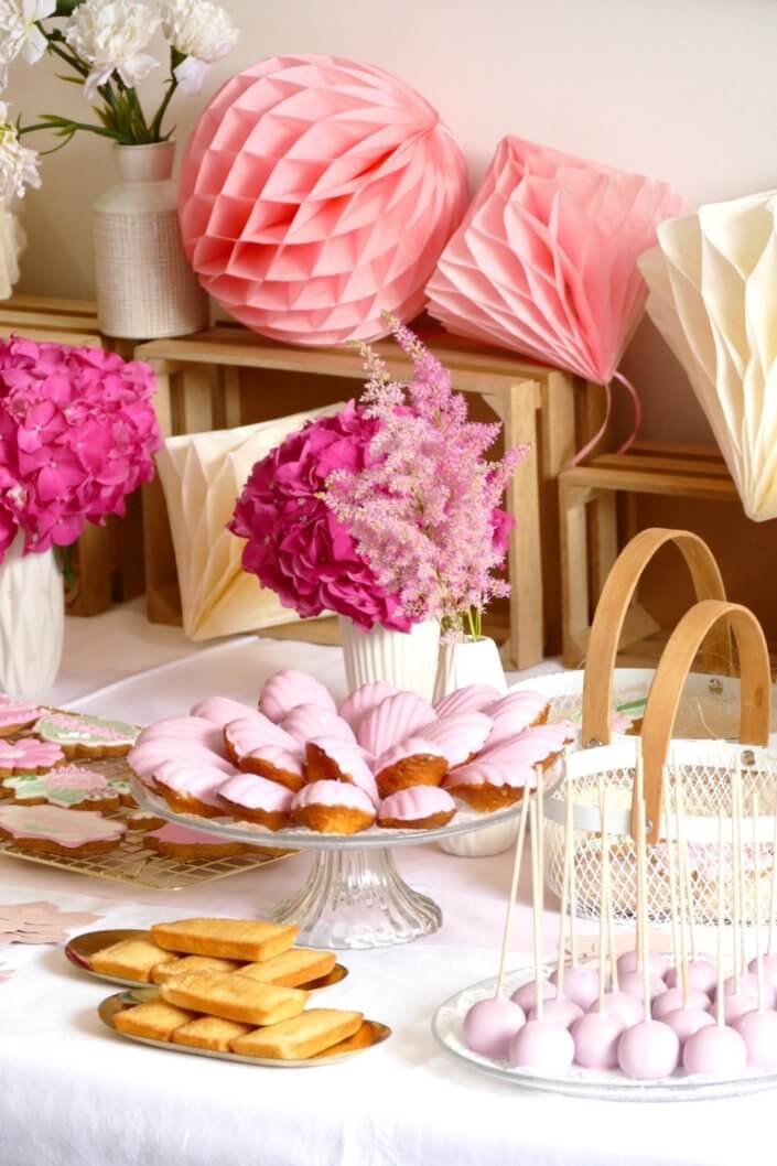 Goûter fleuri en rose et blanc réalisé sur mesure par studio candy avec des pâtisseries personnalisées, mini cupcakes, madeleines à coque rose, gaufres, sablés décorés, et scénographie printanière