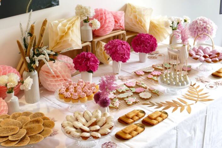 Goûter fleuri en rose et blanc réalisé sur mesure par studio candy avec des pâtisseries personnalisées, mini cupcakes, madeleines à coque rose, gaufres, sablés décorés, et scénographie printanière