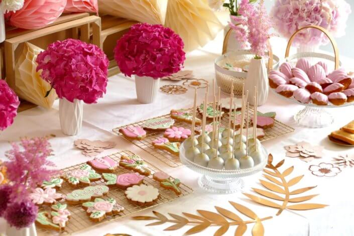 Goûter fleuri en rose et blanc réalisé sur mesure par studio candy avec des pâtisseries personnalisées, mini cupcakes, madeleines à coque rose, gaufres, sablés décorés, et scénographie printanière