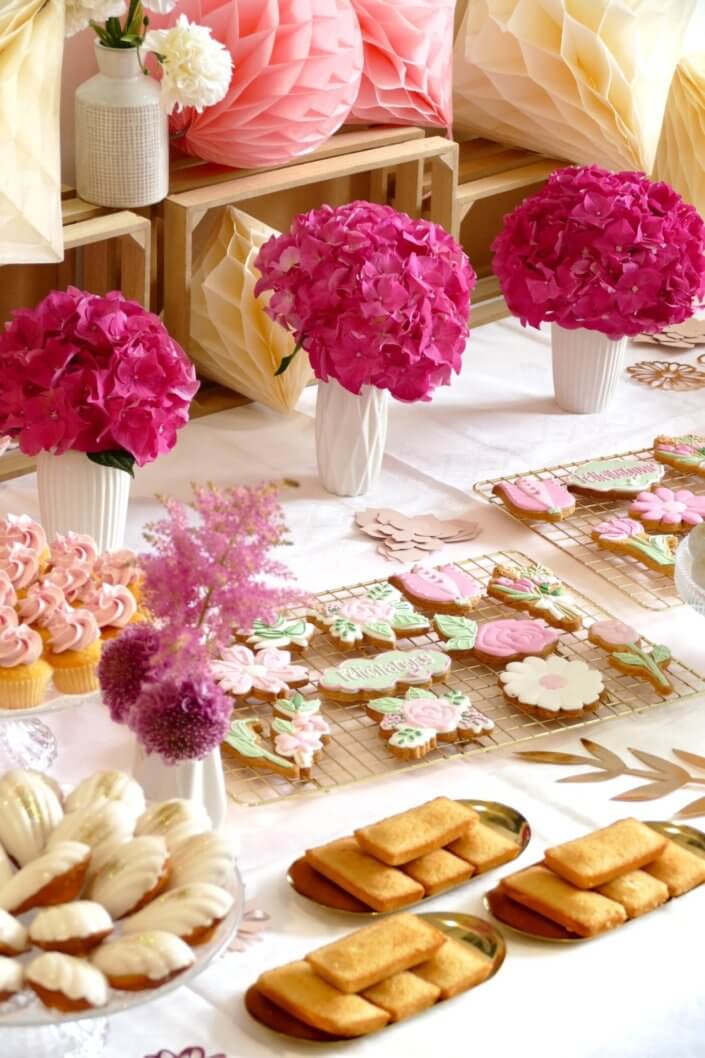 Goûter fleuri en rose et blanc réalisé sur mesure par studio candy avec des pâtisseries personnalisées, mini cupcakes, madeleines à coque rose, gaufres, sablés décorés, et scénographie printanière