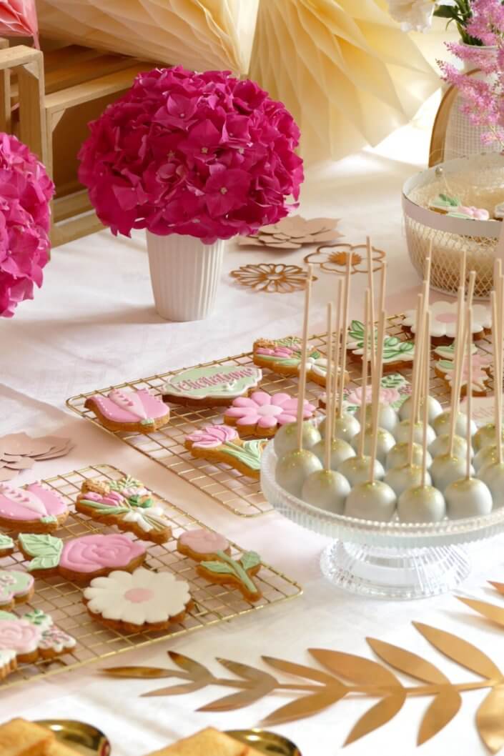 Goûter fleuri en rose et blanc réalisé sur mesure par studio candy avec des pâtisseries personnalisées, mini cupcakes, madeleines à coque rose, gaufres, sablés décorés, et scénographie printanière