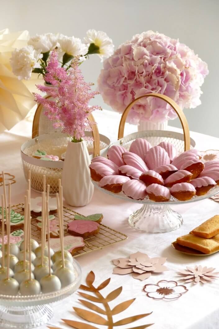Goûter fleuri en rose et blanc réalisé sur mesure par studio candy avec des pâtisseries personnalisées, mini cupcakes, madeleines à coque rose, gaufres, sablés décorés, et scénographie printanière