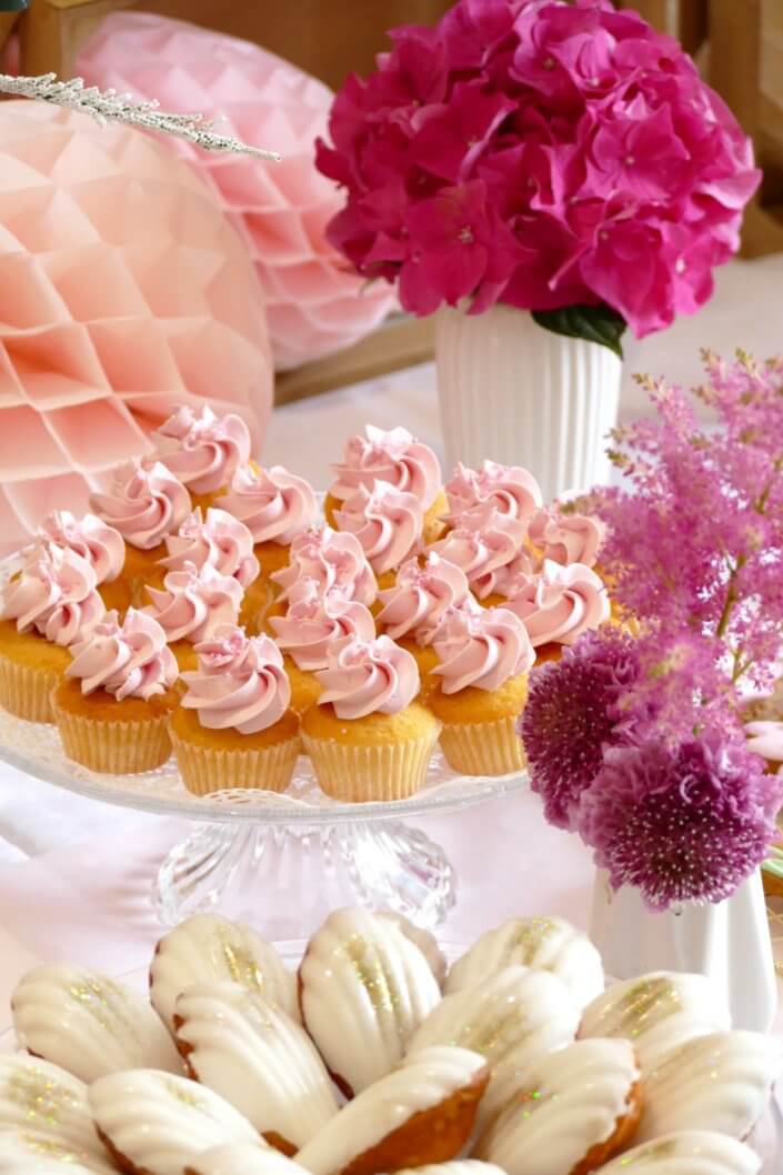 Goûter fleuri en rose et blanc réalisé sur mesure par studio candy avec des pâtisseries personnalisées, mini cupcakes, madeleines à coque rose, gaufres, sablés décorés, et scénographie printanière